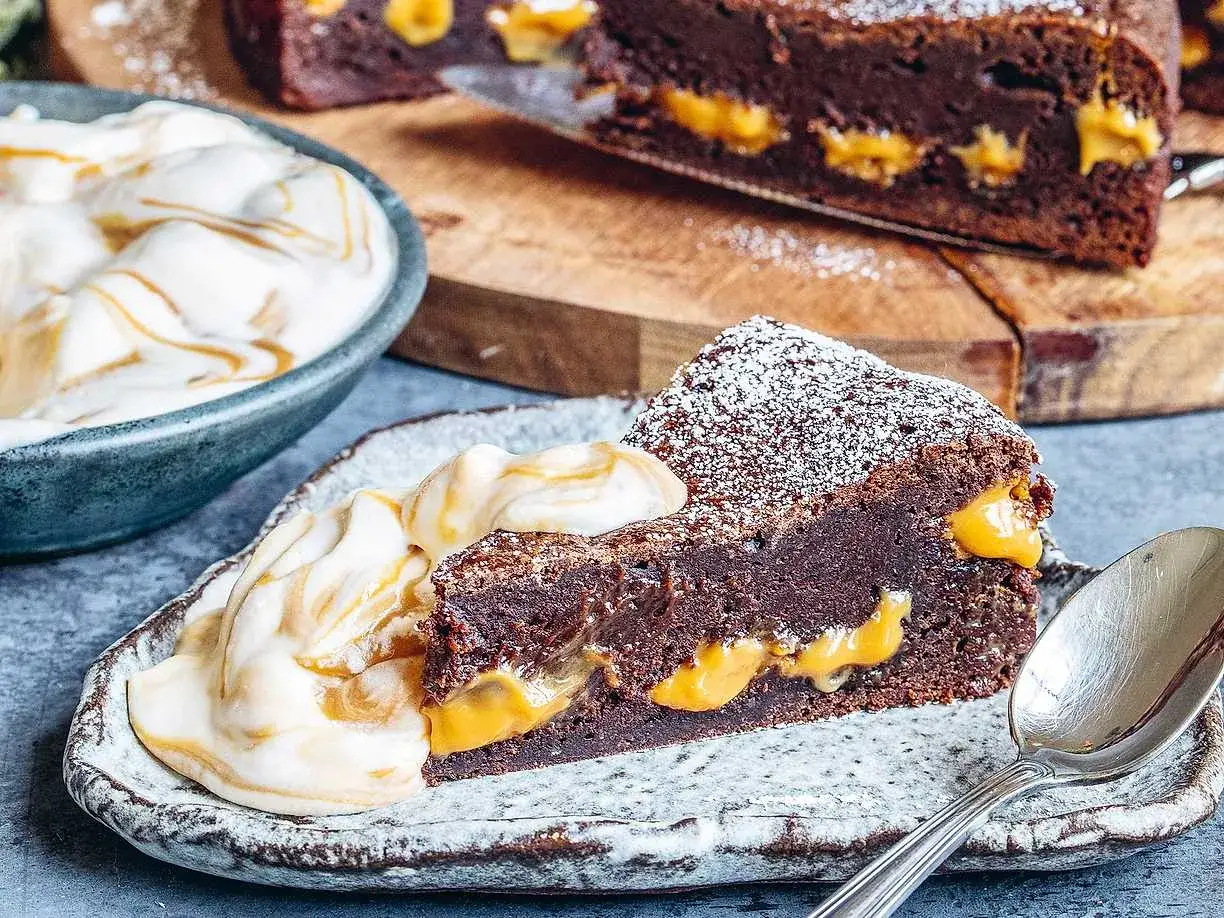 En saftig kladdkaka med len dulce de leche-fyllning, pudrad med florsocker och serverad med vispad grädde.