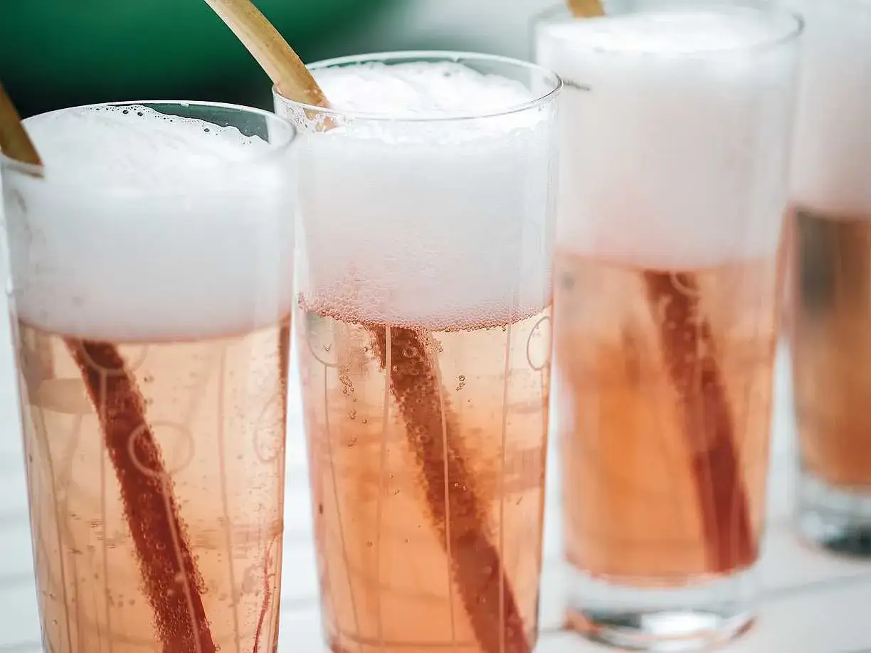 Bubblig rabarbersaft i glas med träpinnar. Perfekt för ett somrigt rabarbersaft recept.
