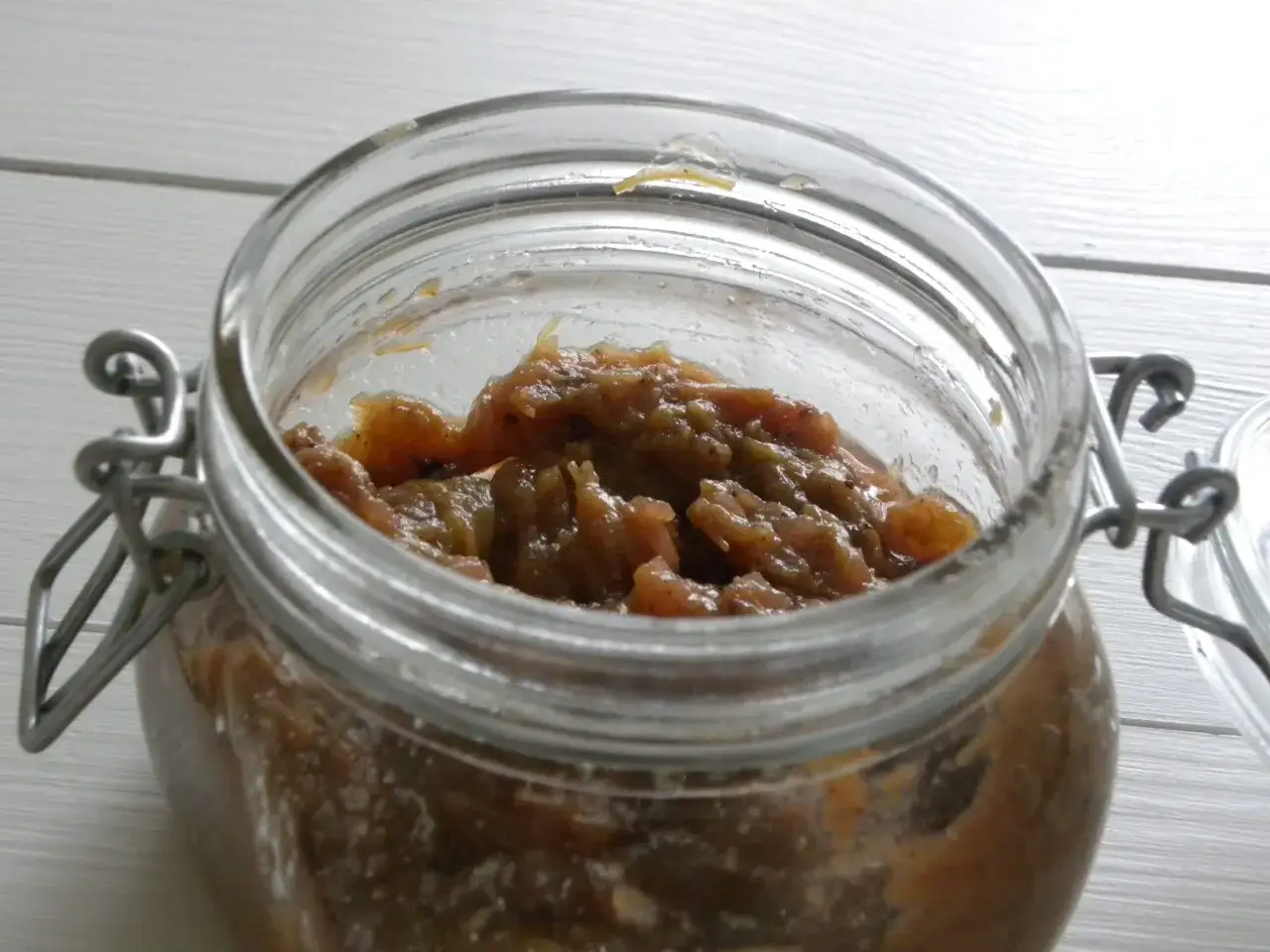 En burk med hemlagad rabarber chutney. Den är fylld med en mustig, brunaktig blandning av rabarber och kryddor.