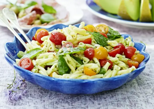 En härlig italiensk pastasallad med körsbärstomater och basilika i en blå skål, perfekt för en sommarlunch.