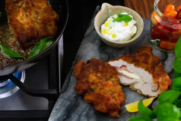 Krispig schnitzel med ost och skinka, serverad med en krämig sås till schnitzel, citron och körsbärstomater.